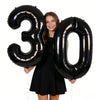 Two black foil balloons shaped like the number 30 held by a smiling woman.