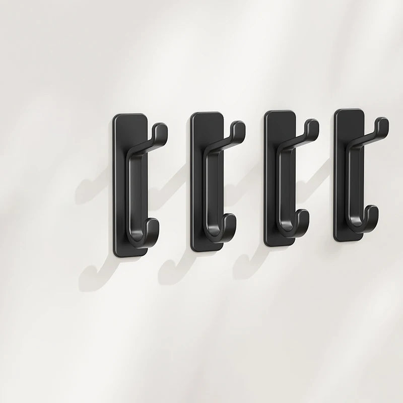 A set of four black self-adhesive wall hooks mounted on a white surface.