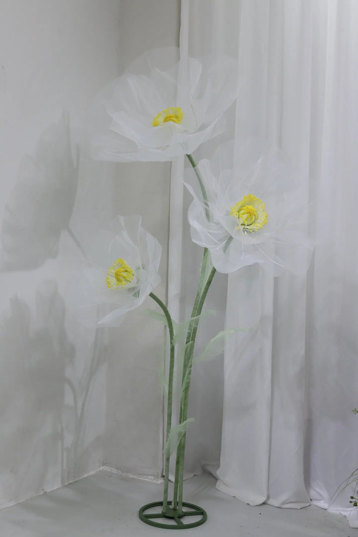 A large artificial silk white poppy flower with a yellow center displayed on a green stand.