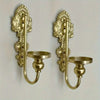 A pair of vintage gold-toned wrought iron wall-mounted candle holders with decorative finials.