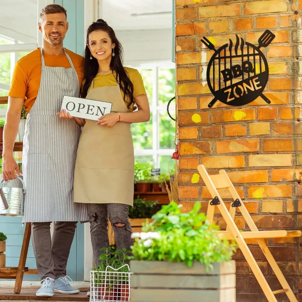 A man and a woman stand in front of a brick wall decorated with a black BBQ ZONE sign.