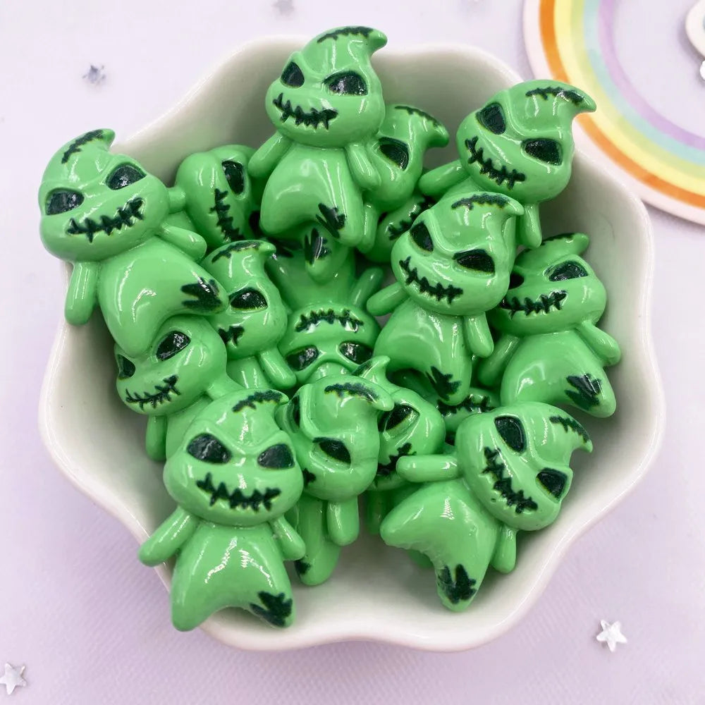 A collection of bright green resin flatback cabochon figurines shaped like grinning, spooky monsters in a white bowl.