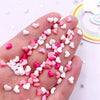 A hand holds a mix of pink and white heart-shaped flatback rhinestones for nail art and crafts.