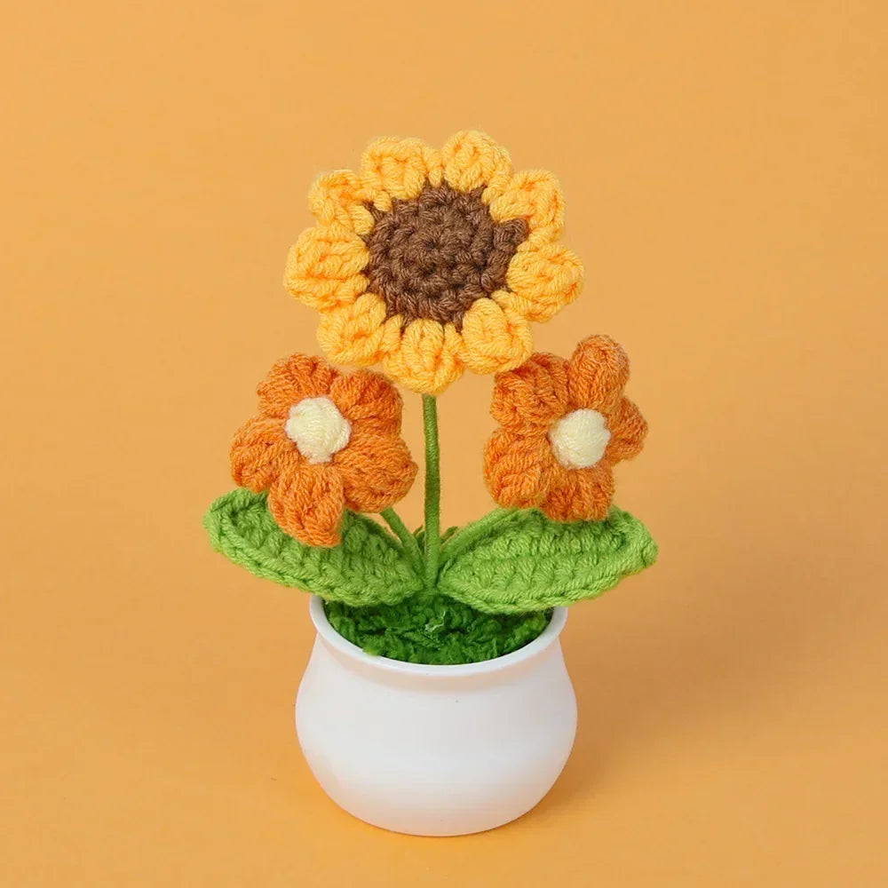 Handmade knitted orange sunflower with a yellow center growing in a white pot.