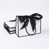 A set of five elegant black and white gift bags tied with black ribbon bows.