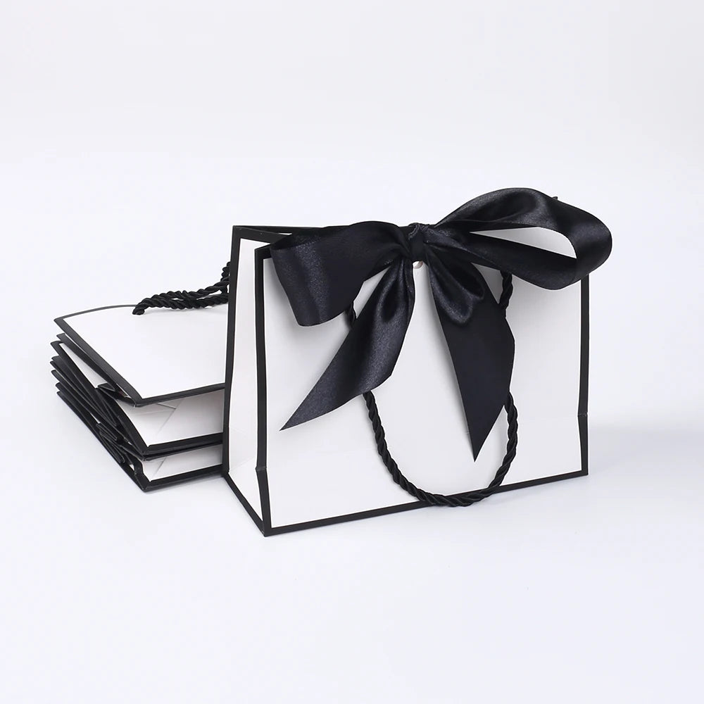 A set of five elegant black and white gift bags tied with black ribbon bows.
