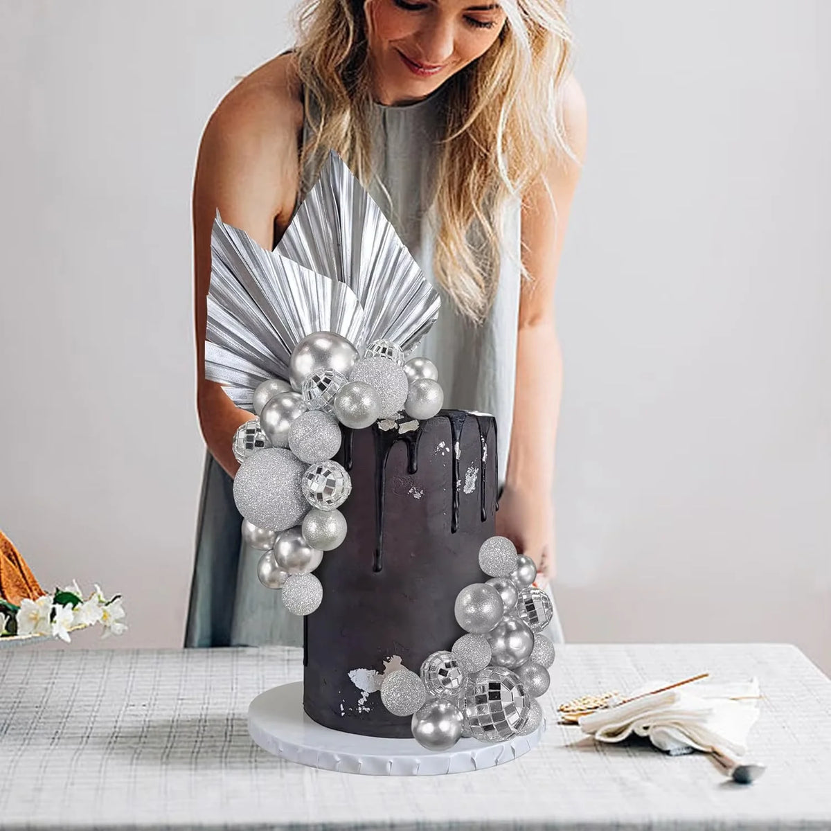 A gray cake decorated with silver disco ball toppers and white flowers on a white table.