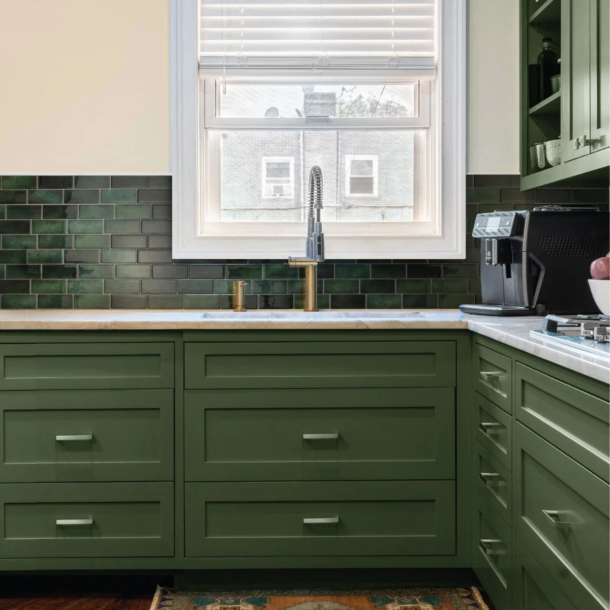 A kitchen cabinet featuring sage green cabinetry and a marble countertop with a window view.