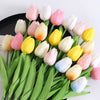 A bouquet of artificial tulip flowers in shades of pink, yellow, and white arranged on green leaves.