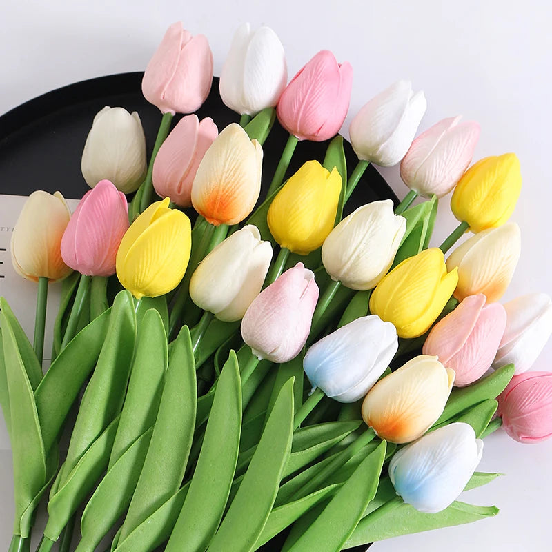 A bouquet of artificial tulip flowers in shades of pink, yellow, and white arranged on green leaves.