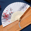 A vintage silk folding hand fan with gray and white stripes and red floral accents resting on a wooden surface.