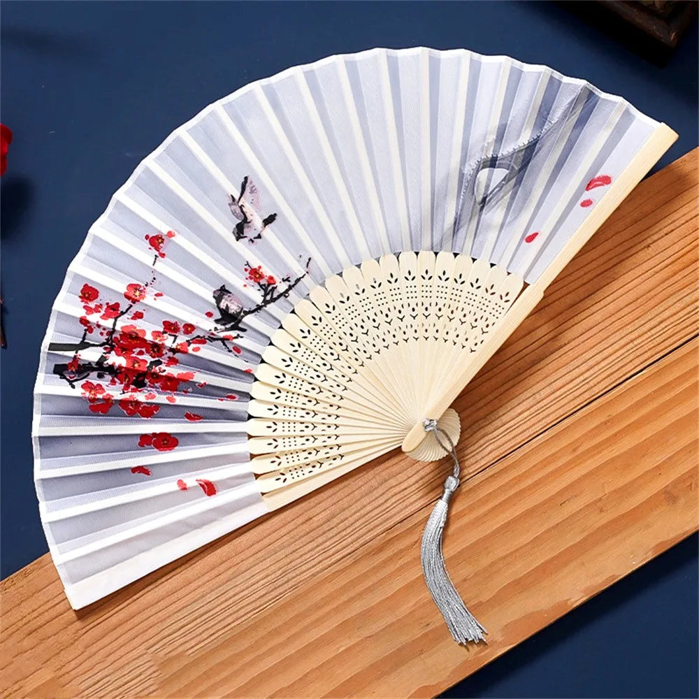 A vintage silk folding hand fan with gray and white stripes and red floral accents resting on a wooden surface.
