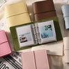 A collection of faux leather photo albums in various shades of green, beige, and pink stacked on a white background.