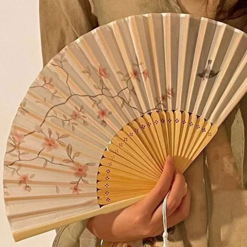 A light wood folding fan with a bamboo frame decorated with delicate pink floral and bird prints.