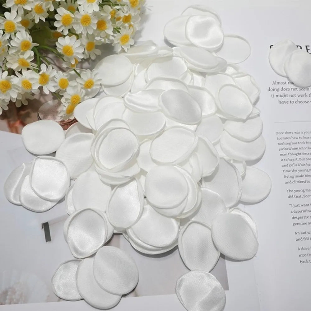 Un amas de pétales de roses en soie artificielle blanches disposés sur une surface blanche.