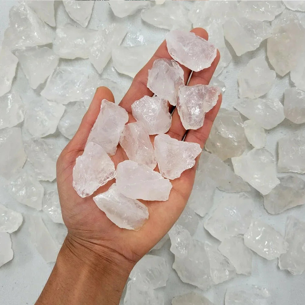 A hand holds several clear pink quartz crystal stones on a white surface.