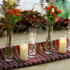 A set of clear glass cylinder vases with dried flowers and fairy lights arranged on a red fabric surface.