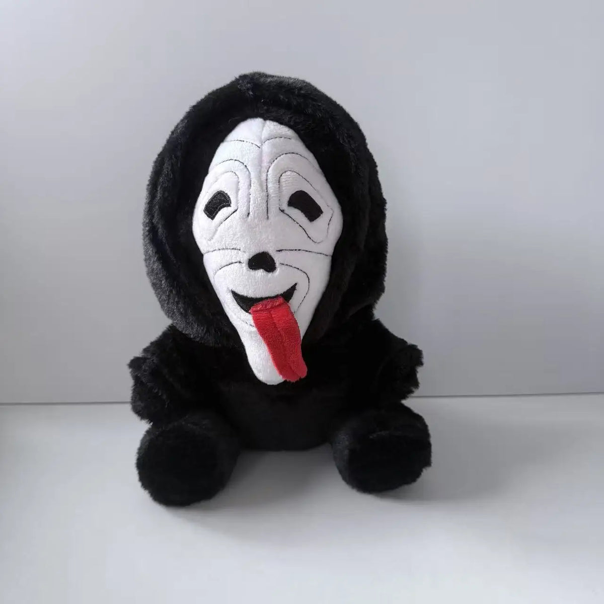 A black plush toy of Ghost Face with a white mask and a red tongue.