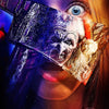 A close-up of a woman's face partially obscured by a menacing knife, featuring a terrifying clown mask and intense blue eyes.