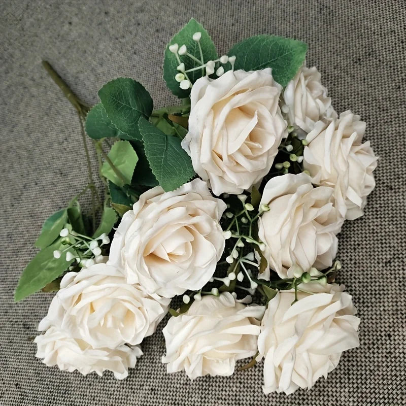 A bouquet of white silk peonies with green leaves and small white filler flowers.