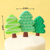 Three green Christmas tree cake toppers with white stripes and leaves on a white cake.