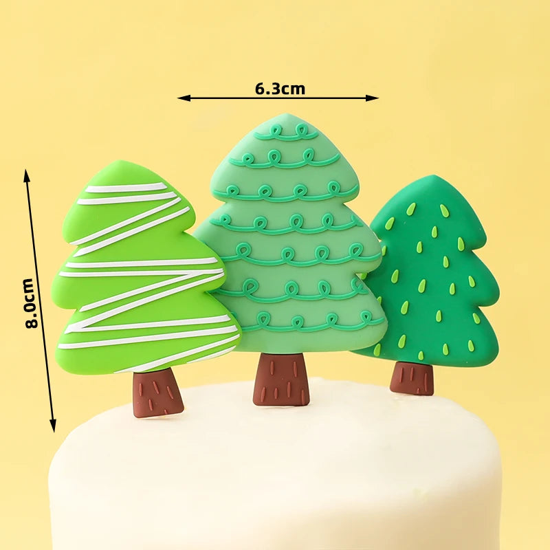 Three green Christmas tree cake toppers with white stripes and leaves on a white cake.