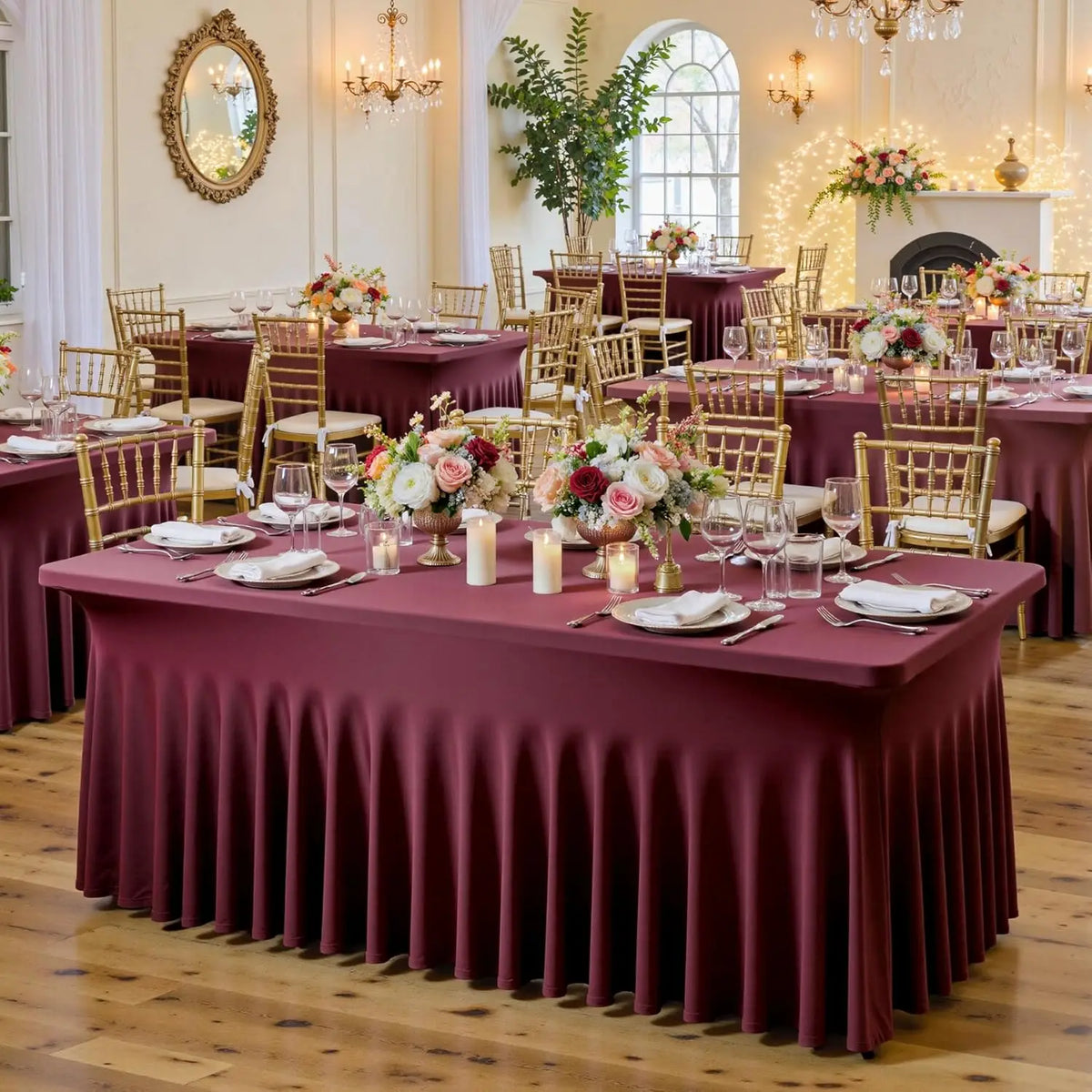A long dining table set for an event with a deep burgundy tablecloth and gold accents.