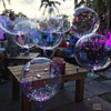 Several clear bubble balloons are floating in the air near people sitting at wooden tables.
