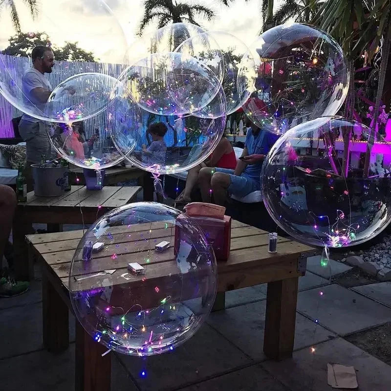 Several clear bubble balloons are floating in the air near people sitting at wooden tables.