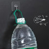 A clear plastic bottle with a green cap is hanging from a self-adhesive wall hook on a dark surface.