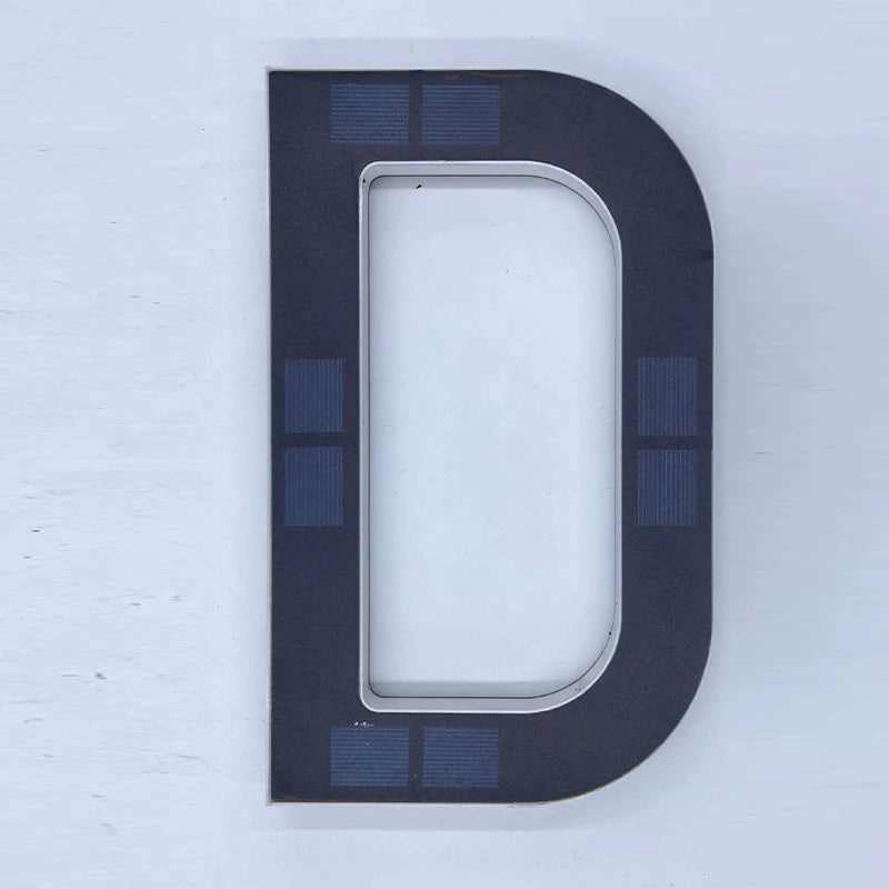 Señal de número de casa ovalada gris oscuro con rectángulo blanco empotrado y pequeños paneles solares azules a los lados.