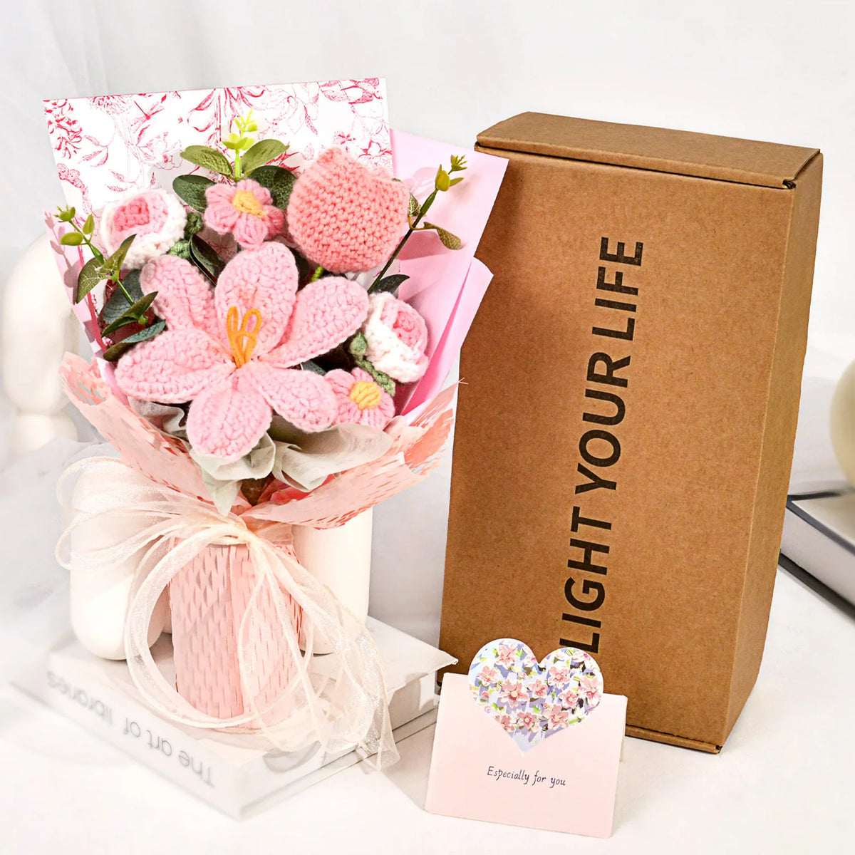 A handmade crochet tulip bouquet with pink and white flowers is displayed next to a brown box labeled Light Your Life.