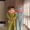 A pair of fuzzy green and blue monster onesie pajamas for couples standing in a room.