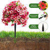 A vibrant pink and red artificial topiary ball flower plant with a black stake, shown against green grass.