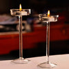 Two elegant tall glass candle holders with lit candles on a white surface.