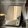 A foldable vanity mirror with an adjustable stand is shown on a table next to a glass and a candle.