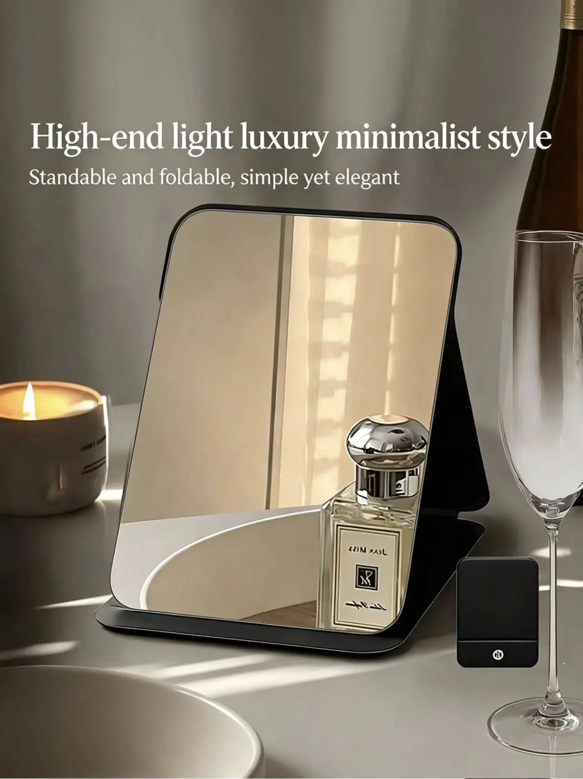 A foldable vanity mirror with an adjustable stand is shown on a table next to a glass and a candle.