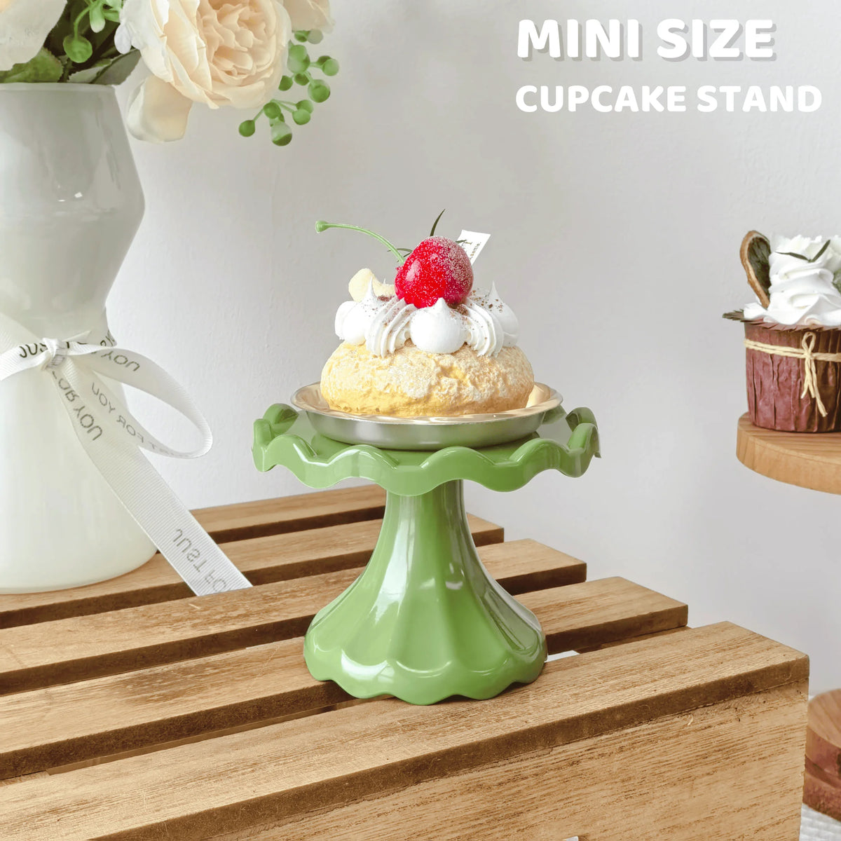 A mini green cupcake stand displaying a decorated cupcake with cream and a strawberry on a wooden surface.