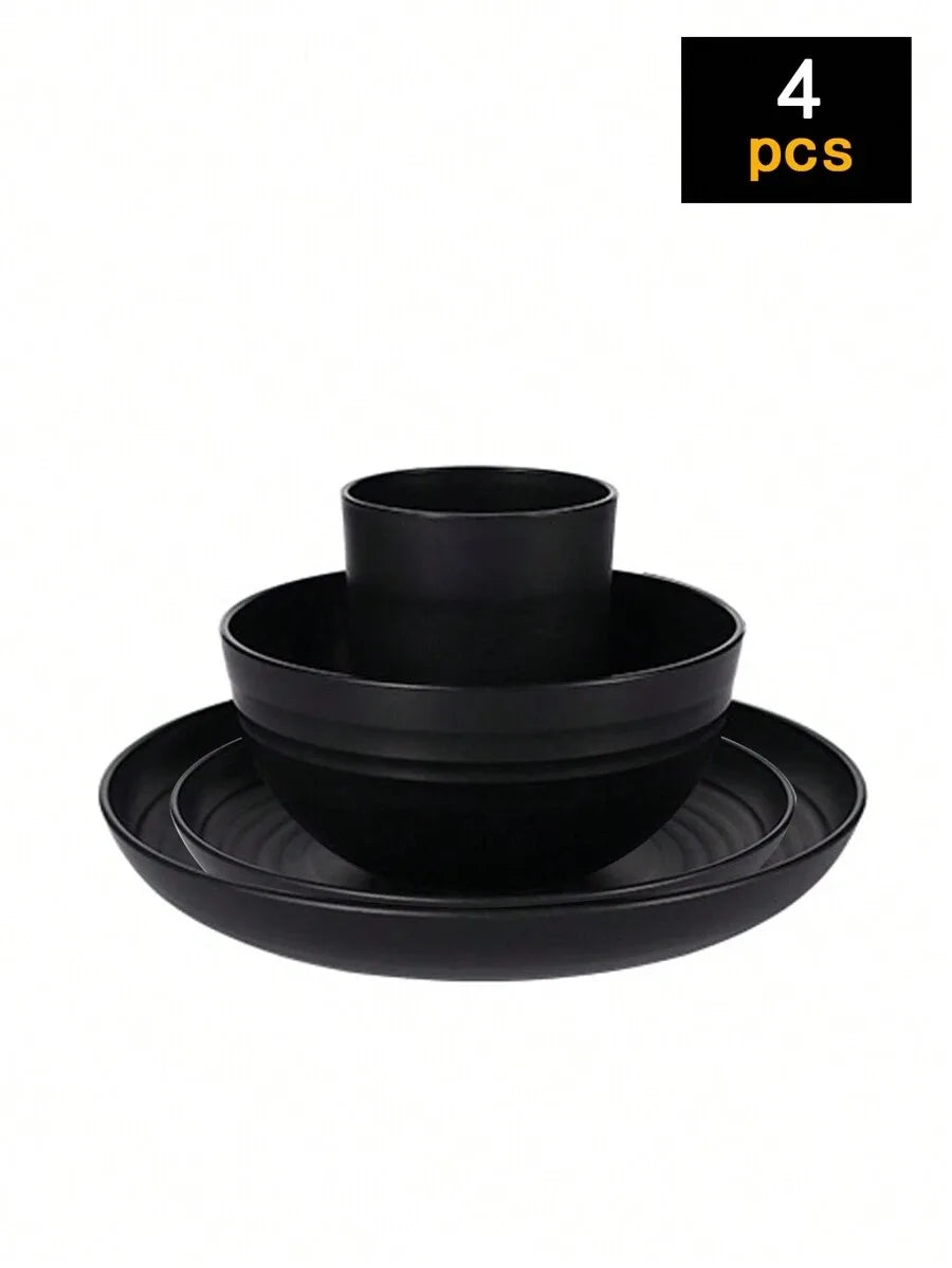 A set of four black reusable plastic tableware items including a bowl and plates.