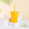 A bright orange plastic cold cup with a yellow lid and straw is displayed on a white surface.