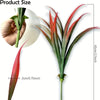 A vibrant red and green artificial tall grass plant with long, pointed leaves shown next to a hand for scale.