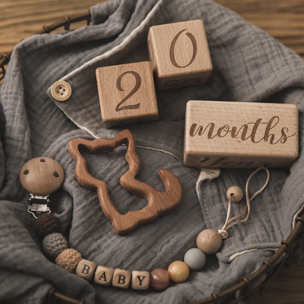 A collection of wooden baby milestone cards and a wooden silhouette necklace displayed on a gray linen cloth.