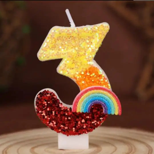 A decorative candle shaped like the number 3, featuring yellow and orange sequins, resting on a white base.