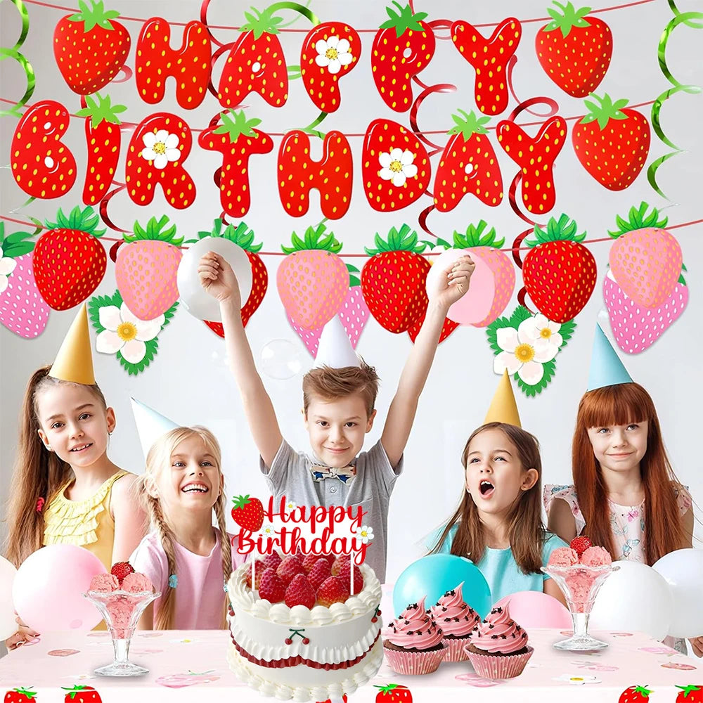 A colorful strawberry birthday party decoration set featuring banners, cake toppers, and cupcakes on a table.