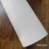 A roll of pale pink self-adhesive 3D linen texture wallpaper panels lying on a dark wood floor.
