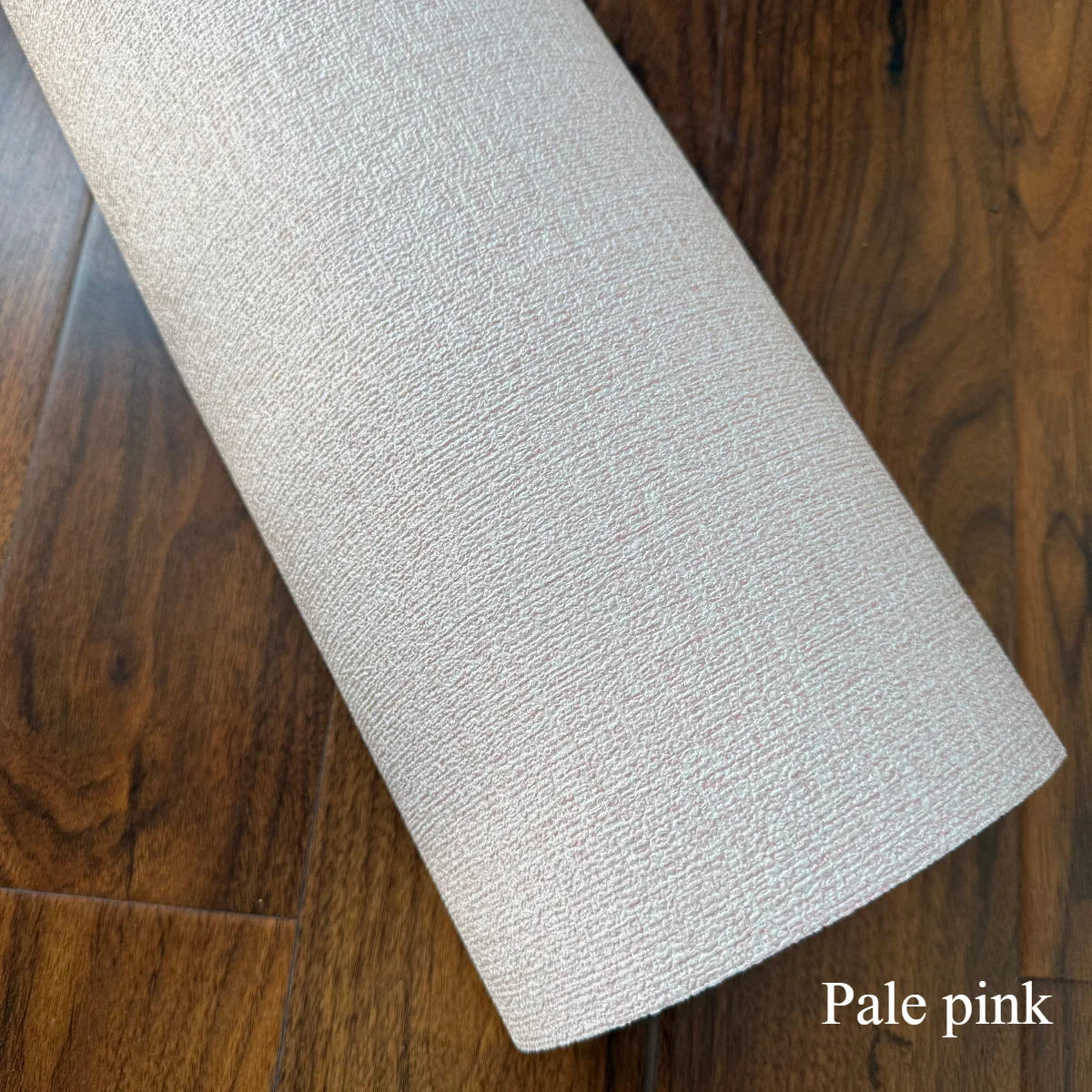A roll of pale pink self-adhesive 3D linen texture wallpaper panels lying on a dark wood floor.