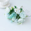 A bouquet of artificial silk peony flowers in soft blue and white tones arranged on a white surface.