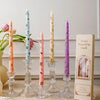 A collection of decorative printed long stick candles in various colors and floral patterns displayed on a light surface.