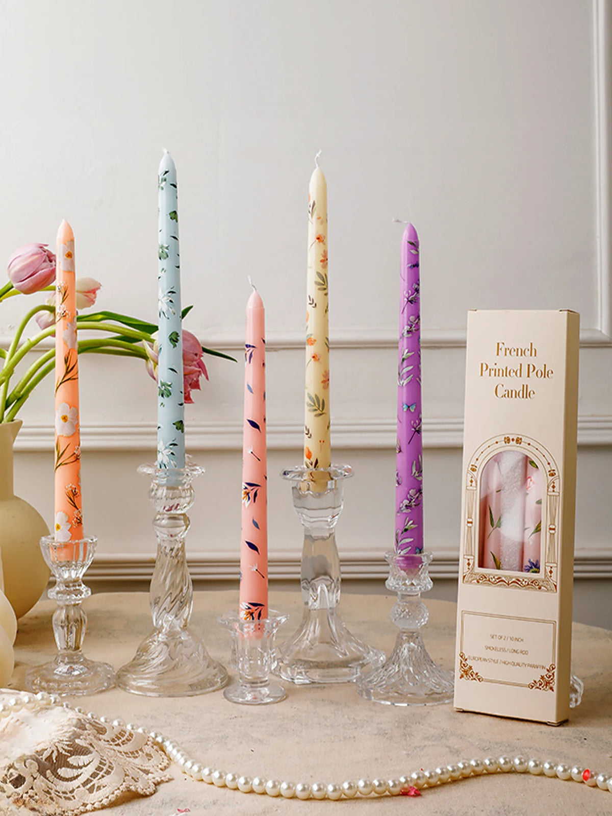 A collection of decorative printed long stick candles in various colors and floral patterns displayed on a light surface.