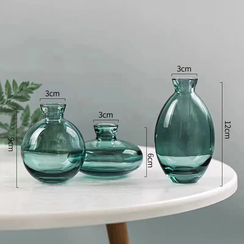 A set of three clear glass mini vases with varying sizes and neck diameters displayed on a white surface.